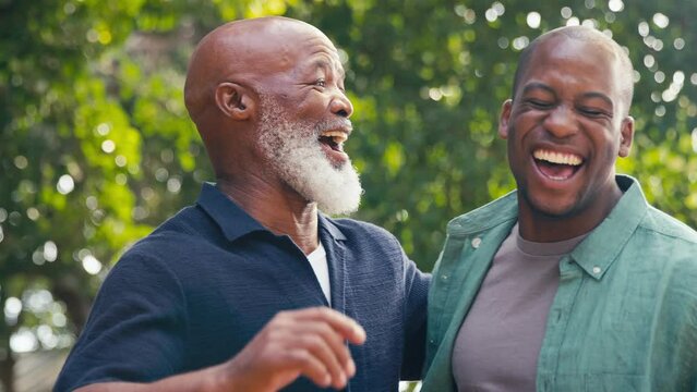 Family shot with senior father talking and laughing with adult son outdoors in countryside - shot in slow motion