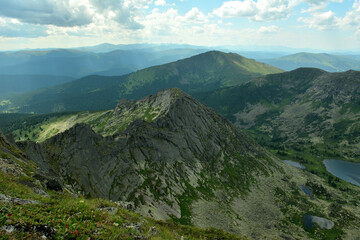 A fragment of a picturesque lake and its high pointed peaks surrounded by a summer cloudy sky.