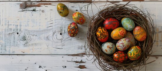 Easter eggs adorned with wax-resist dyeing method, known as Pysanky, displayed in a nest on a white wooden surface. The style is a traditional craft popular in Eastern European regions, - obrazy, fototapety, plakaty