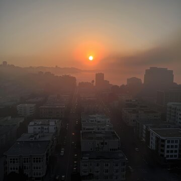 Sunrise over cityscape shrouded in morning fog - A breathtaking sunrise over a cityscape covered in morning fog, depicting the start of a new day