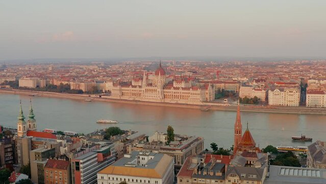 Panoramic view of the Hungarian Parliament Building during a pink sunset. Buda and Pest separated by the Danube River. Boat crossing the Danube River. Famous Hungarian landmarks, Budapest skyline.