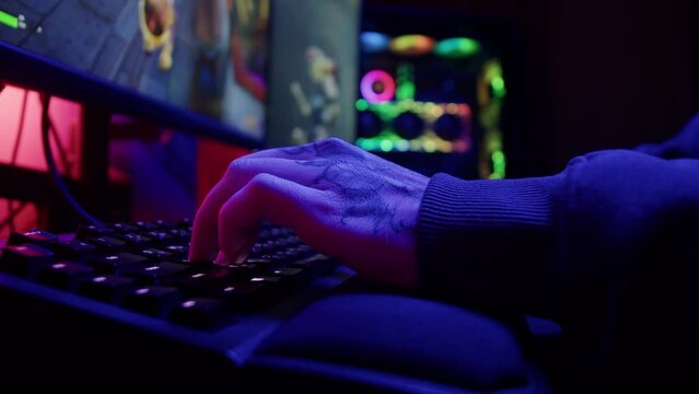 Gamer typing on backlight keyboard close-up, man playing video game in blue neon light . Male hands pushing buttons on computer mouse. having a stream, cyberspace.