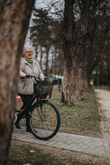 Mature female retiree with glasses and casual attire takes a break from cycling in a serene park setting.