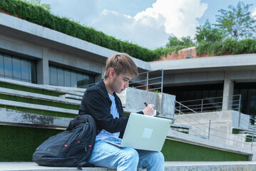 Asian male student sitting and watching and using a computer notebook to review the lesson on people and adult education concepts.