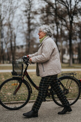 Active senior female retiree with glasses and a smile walking her bicycle through a tranquil park setting.