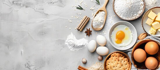 Baking ingredients like flour, eggs, butter, and kitchen textiles laid out on a bright grey concrete background for a cookies, pie, or cake recipe mockup with copy space in top view.