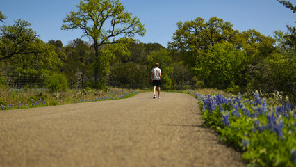 Obraz premium Man walking down a road lined with Texas Bluebonnets