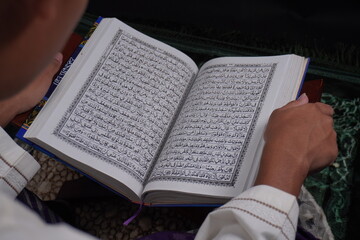 person reading holy quran on rug with isolated dark background