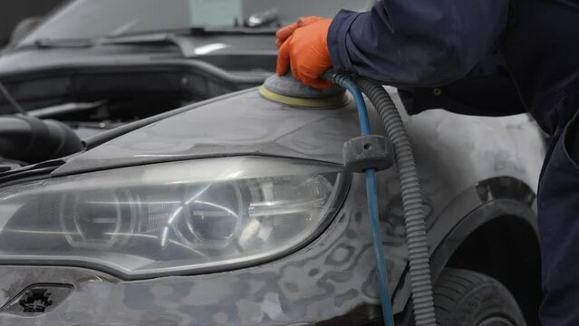 A mechanic sands the putty on a car body with a machine. Repair after an accident. 