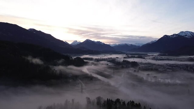 Drone fly above misty pine forest with Aerial Drone View over cityscape in Frastanz, Austria, Sunrise above foggy winter mountain landscape