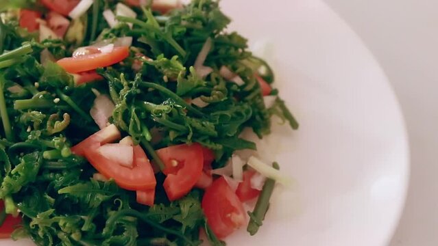 Close up overhead shot of  seasoning grains dropping to a plate of fiddlehead fern or pako salad, a local Filipino delicacy showing the authentic daily home life and heritage