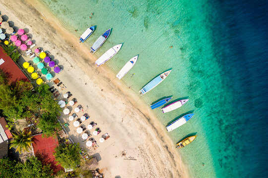 Top down view of colorful sunshades and tourist boats on a tropical beach
