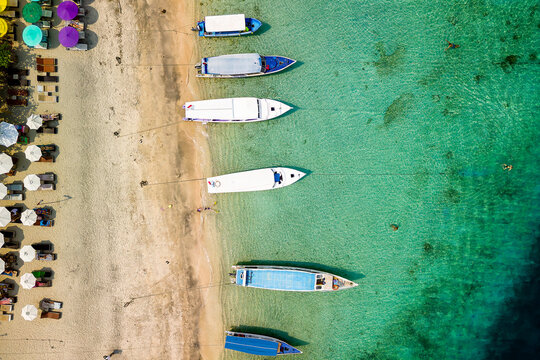 Birds eye view of colorful sun umbrellas and boats on a small, warm tropical beach