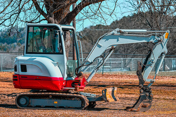 Red and white mini excavator after doing dirt work parked by a tree. © Micah Tanner
