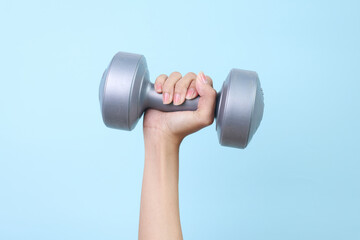 Woman's hand holding grey dumbbell isolated on blue background. Equipment for home workout.