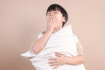 Young Boy In Pajamas Holding Pillow While Yawning Isolated on Beige Background