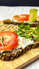 Rye bread bruschettas with cottage cheese on a wooden kitchen board are decorated with vegetables and herbs. Shooting from a large angle in close-up. Healthy food.