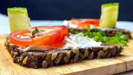 Bruschetta with cottage cheese slices of tomato and cucumber on a wooden board with herbs and sunflower seeds. Close-up shooting.