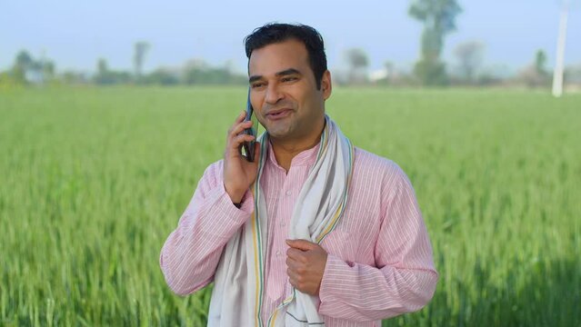 Desi Indian farmer talking on phone in his field - village lifestyle  labor  unskilled labor  looking for work. Closeup shot of a village man in kurta pajama talking with family on phone call - use...