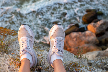 Travel and tourism. Female legs in white sneakers hanging from a rocky shore on the sea coast