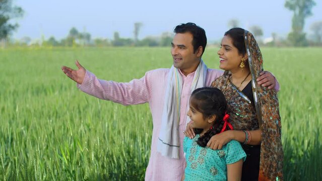 Desi Indian farmer happily showing his farmland to his family - village lifestyle  rural area  farming  farms. Happy villager family enjoying the green environment of the farms - agriculture  carin...