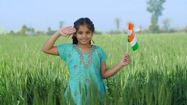 Young Indian girl proudly saluting the nation - proud Indian  nation lover  desh prem  national holiday. Rural girl saluting while holding tri color national flag before independence day celebratio...