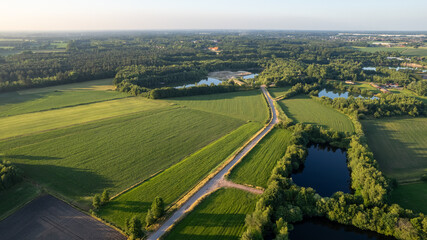 This aerial image showcases a sprawling rural landscape during the golden hour, with the low angle of the sunlight casting a warm glow over the scene. The composition divides the frame into a mosaic