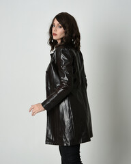 close up portrait of beautiful brunette woman wearing long black leather trench coat, film noir detective. Standing pose in side profile, looking back over shoulder,  Isolated on studio background