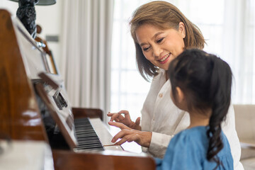 Portrait of happy love asian grandmother and asian cute girl play and enjoy relax teaching and play piano music lesson at home.senior, insurance, care.girl with their laughing grandparents.Family
