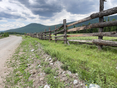Old wooden fence on the road in the mountains. Summer landscape.