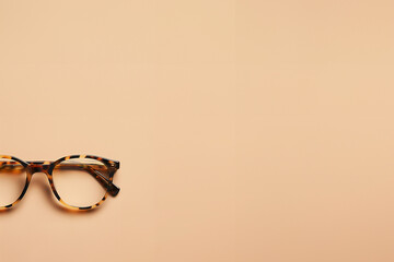 paire de lunettes de vue avec une monture classique type écailles de tortue. Accessoire de bureau ou pour étudiant, opticien sur un fond beige orangé avec espace négatif copy space.