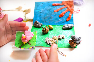 Child smearing colorful plasticine on cardboard and creating fairy tale card with cartoon animals