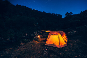 tents pitched on hillsides beside streams of water from waterfalls at night under star in the sky.