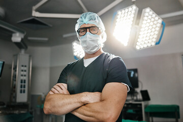 Surgery, portrait and arms crossed by man doctor in operating room with confidence in medical,...