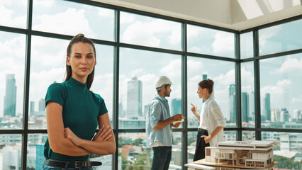Young beautiful interior designer crossing arms while engineer team talking about house design. Skilled businesswoman smiling at camera with confident while sitting near house model. Tracery - obrazy, fototapety, plakaty