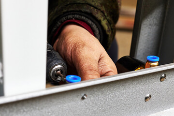 hand of a worker screwing a product with electric screwdriver to a metal bar