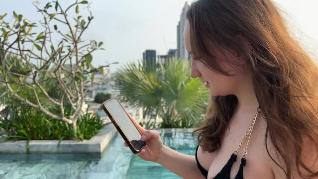 Woman freelancer sits on deck chair near pool and works on laptop. Girl uses laptop for remote work on vacation and receives good news by email. High quality 4k footage