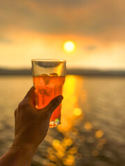 hand holding a glass of orange lemonade in front of a sunset over water