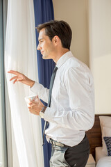 Handsome young businessman drinks coffee in front of the hotel window - 767662857