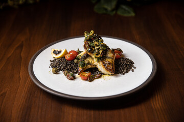 grilled fish with lentils and vegetables served in dish in restaurant on dark background