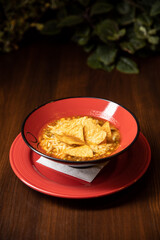 mexican tortilla soup served in red dish in restaurant with red cocktail on dark background