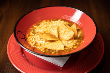mexican tortilla soup served in red dish in restaurant with red cocktail on dark background