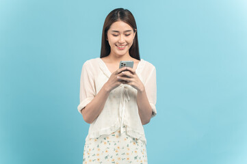 Beautiful young asian woman in white dress with flower pattern using smartphone isolated on blue background