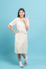 Beautiful young asian woman in white dress with flower pattern making okay sign isolated on blue background
