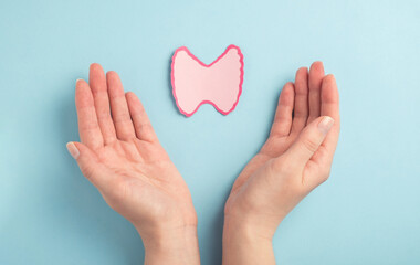 Thyroid gland decorative model in woman hands on pastel blue background. Hyperthyroidism, Hypothyroidism, thyroid cancer awareness concept. Top view