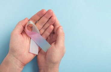 Thyroid gland cancer awareness concept. Man holding colorful ribbon on pastel blue background. Top view, copy space