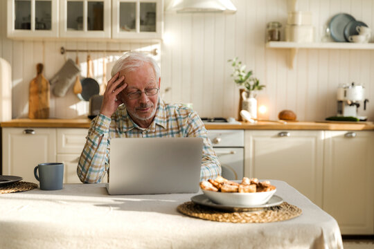 elderly grey haired man in eyeglasses try to deal with laptop alone