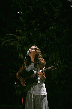 Young woman singer, sings into a microphone and plays the guitar.