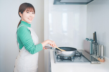 キッチンでフライパンを使って料理する女性