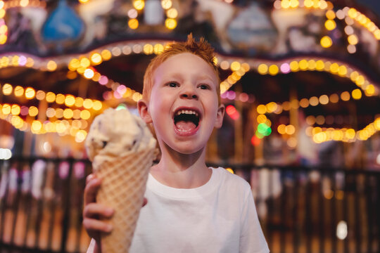 Young smiling boy holding an ice cream cone with ferris wheel